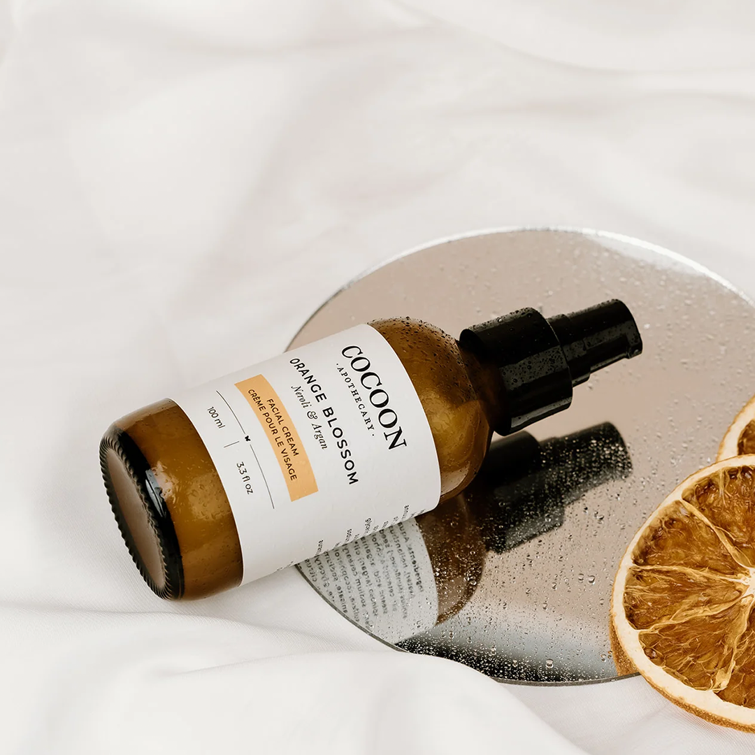 image: a bottle of cocoon apothecary's orange blossom facial cream lying on its side.