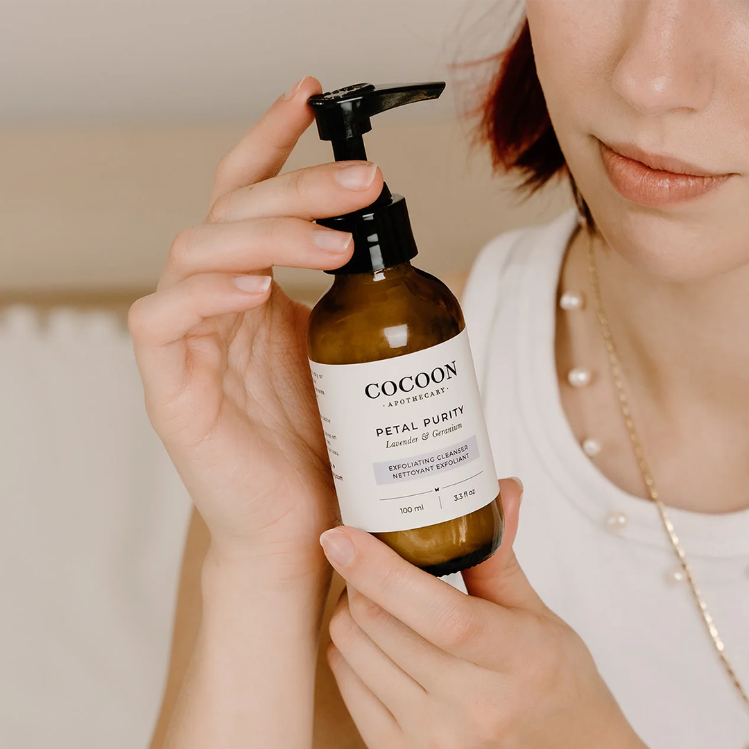  image: a bottle of cocoon apothecary's petal purity exfoliating cleanser held by a model