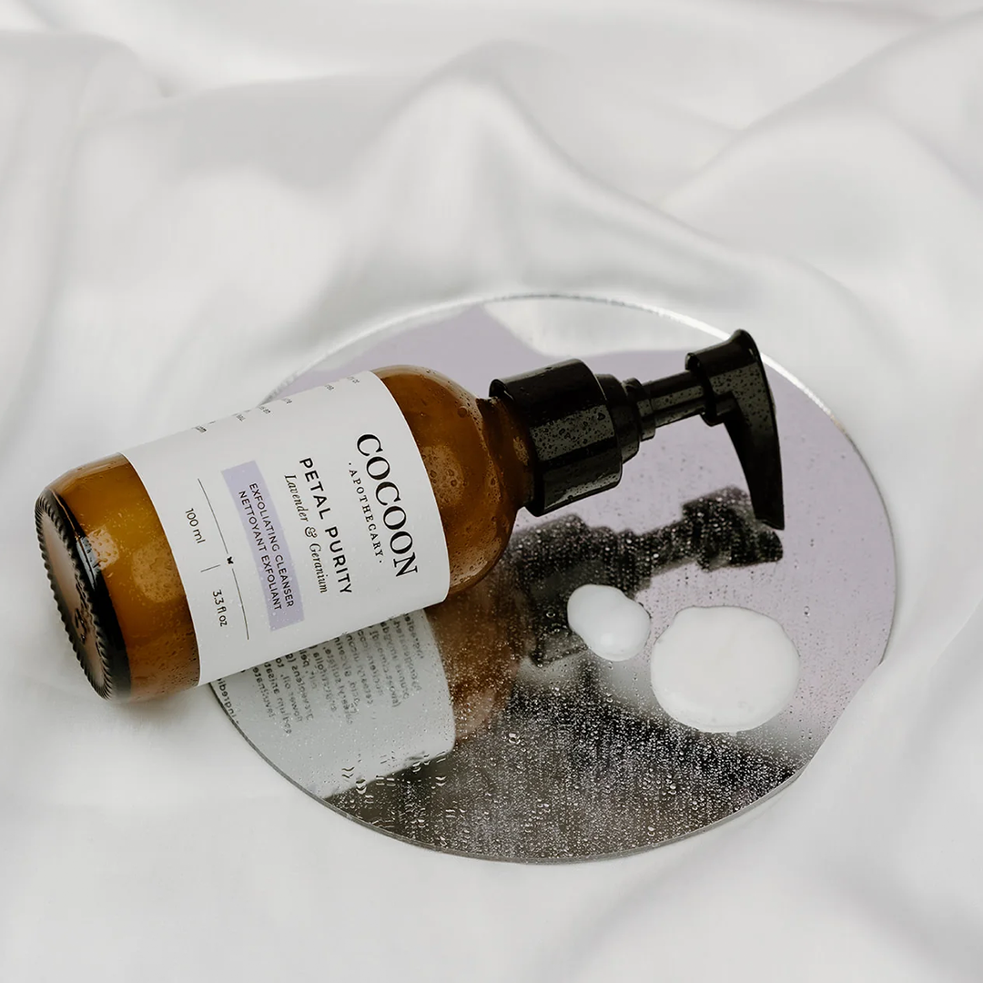  image: a bottle of cocoon apothecary's petal purity exfoliating cleanser lying on it's side on a mirror